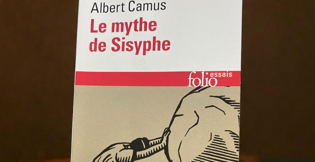 Un homme pousse un rocher sur une pente escarpée sous un ciel bleu méditerranéen, métaphore de Sisyphe chez Camus